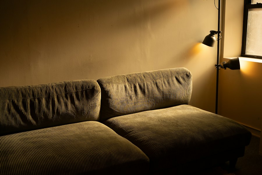 An olive corduroy sofa lit by a wall lamp in the evening
