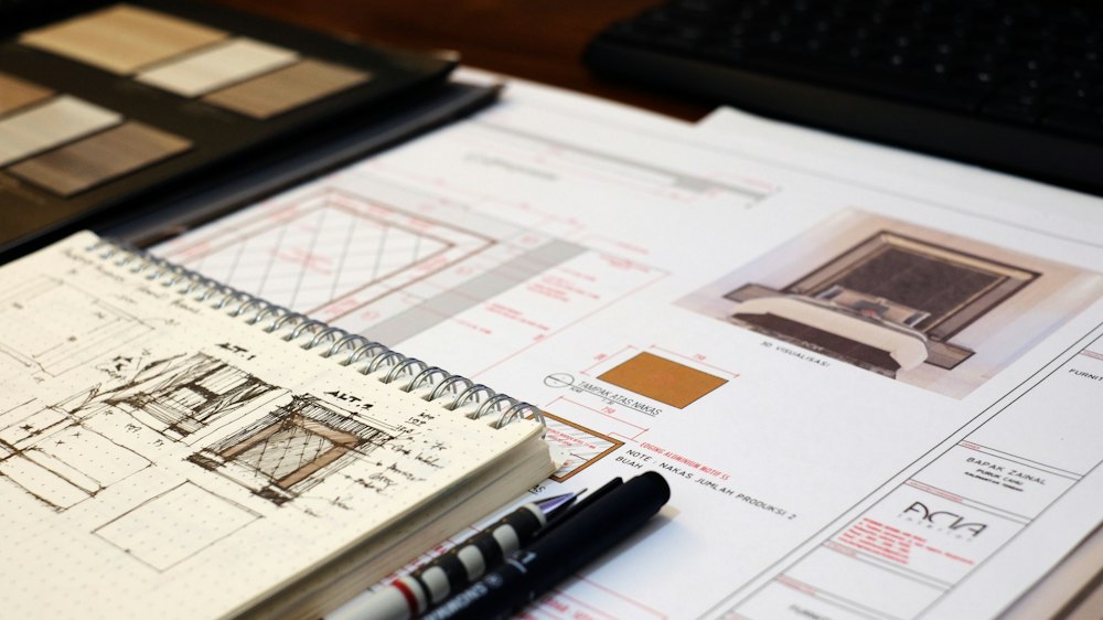 Interior elevation drawings on a desk beside a tray of finish samples